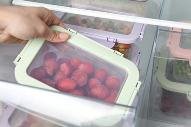 Photo of Woman taking box with frozen strawberry from refrigerator, closeup