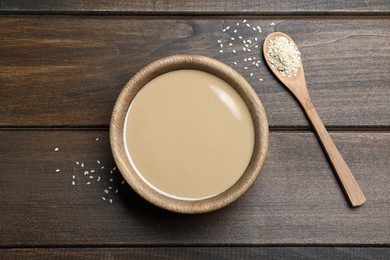 Tasty sesame paste, seeds and spoon on wooden table, flat lay