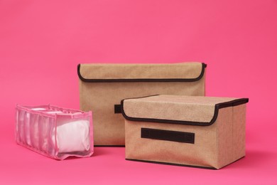 Textile storage cases and organizer with folded clothes on pink background