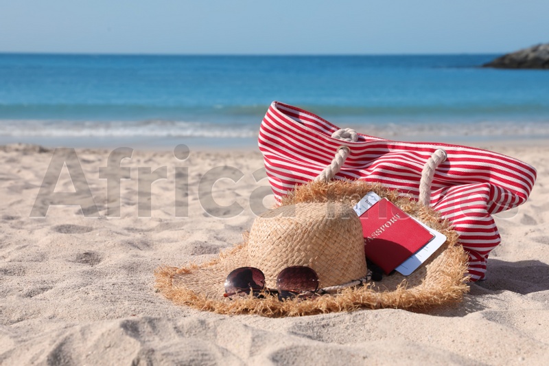 Photo of Straw hat with sunglasses, bag, passport and ticket on sandy beach