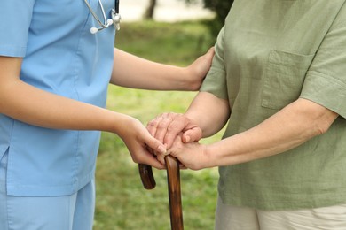 Elderly woman with walking cane and female caregiver outdoors, closeup