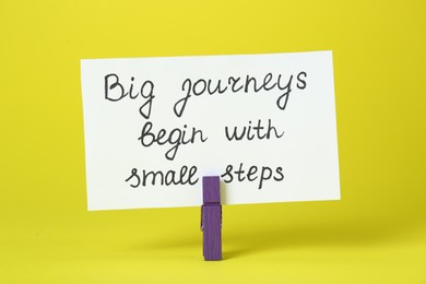 Photo of Card with phrase Big Journeys Begin With Small Steps and clothespin on yellow background. Motivational quote