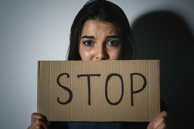 Abused young woman with sign STOP near white wall. Domestic violence concept