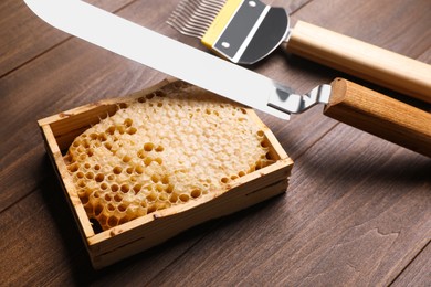 Honeycomb frame and beekeeping tools on wooden table, closeup