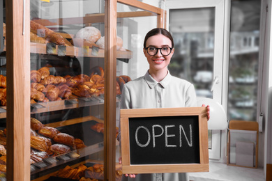 Female business owner holding OPEN sign in bakery