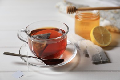 Tea bags, honey and lemon near cup of hot drink on white wooden table, closeup. Space for text