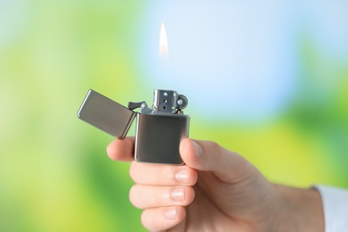 Man holding lighter with burning flame against blurred green background, closeup