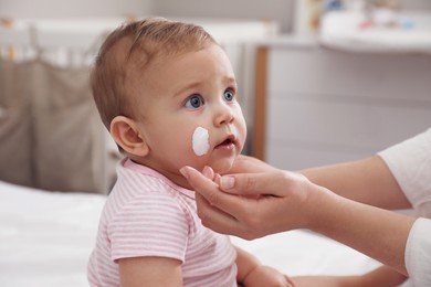 Mother applying moisturizing cream on her little baby at home, closeup