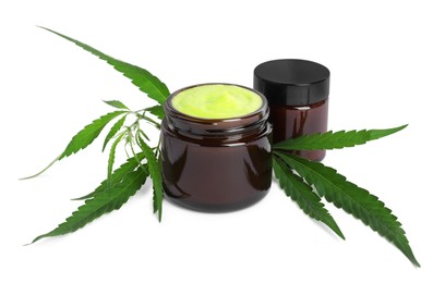 Jars with hemp cream and green leaves on white background. Natural cosmetics