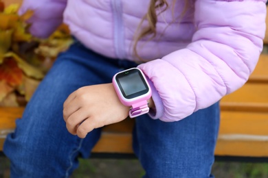 Little girl with stylish smart watch on bench outdoors, closeup