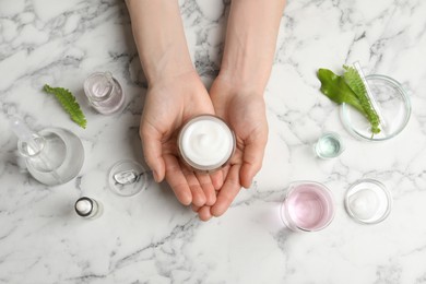 Woman holding jar of cosmetic product at white marble table, top view