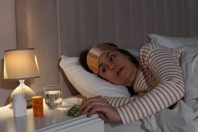 Mature woman taking pills from nightstand in bedroom at night. Insomnia concept