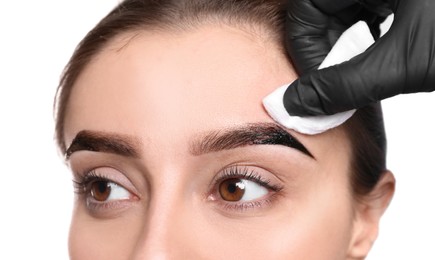 Beautician wiping tint from woman's eyebrows on white background, closeup