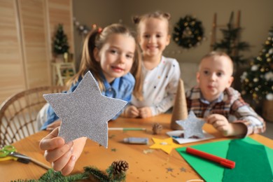 Cute little children at table indoors, focus on hand with star. Making Christmas decor
