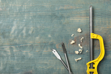 Small hand saw, spade drill bits and shavings on blue wooden background, flat lay with space for text. Carpenter's tools