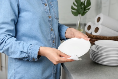 Woman wiping ceramic plate with paper towel indoors, closeup