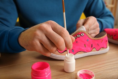 Man painting on sneaker at wooden table indoors, closeup. Customized shoes