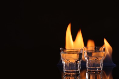 Vodka in glasses and flame on black background, space for text