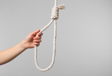 Woman holding rope noose on light grey background, closeup. Space for text