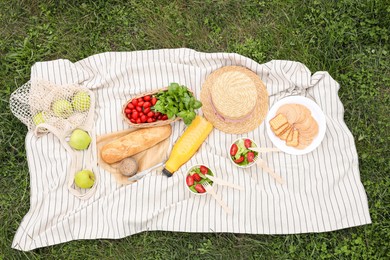 Picnic blanket with juice and food on green grass, top view