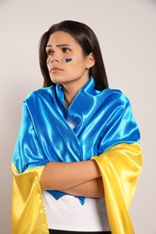 Photo of Sad young woman with face paint and Ukrainian flag on beige background