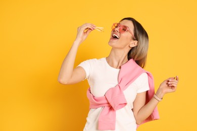 Young woman eating French fries on yellow background. Space for text