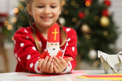 Cute little girl with paper Saint Nicholas toy at home, focus on hands