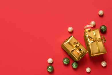 Photo of Gift boxes and Christmas balls on red background, flat lay. Space for text