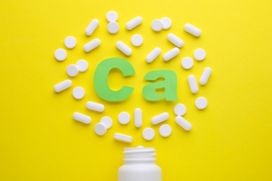 Pills, open bottle and calcium symbol made of green letters on yellow background, flat lay