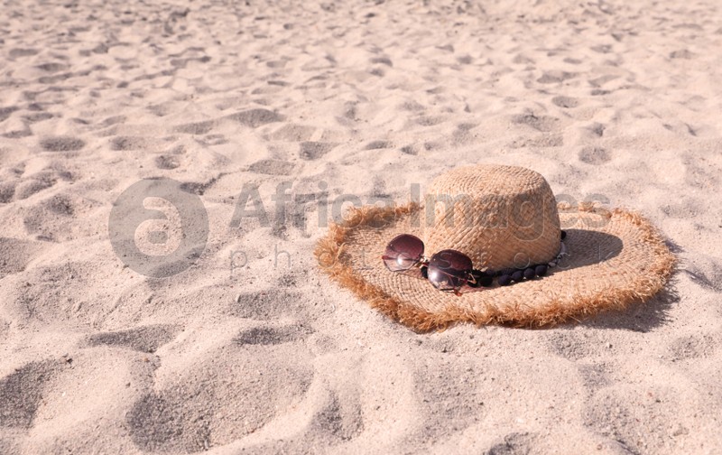 Photo of Straw hat with sunglasses on sandy beach. Space for text