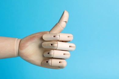 Wooden mannequin hand showing thumb up on light blue background. Space for text