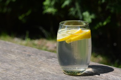 Refreshing water with lemon on wooden table outdoors, space for text