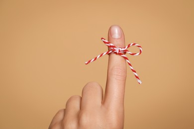 Woman showing index finger with tied bow as reminder on light brown background, closeup
