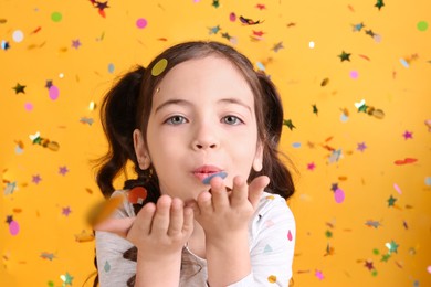 Adorable little girl blowing confetti on yellow background