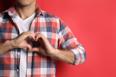 Photo of Man making heart with hands on red background, closeup. Space for text