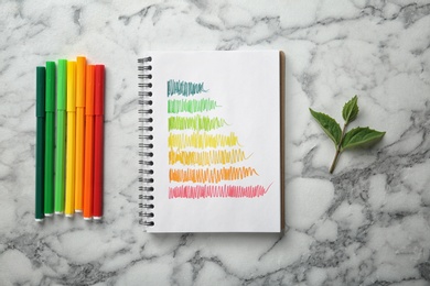 Notebook with colorful bars and markers on white marble background, flat lay. Energy efficiency rating chart