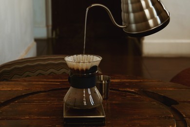 Pouring water from kettle into cup with coffee and wave dripper in cafe, closeup