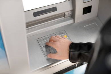 Man entering PIN code on cash machine keypad outdoors, closeup view