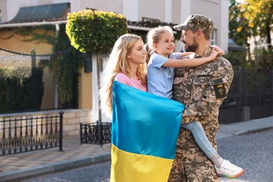 Photo of Soldier in military uniform reunited with his family and Ukrainian flag on city street, space for text