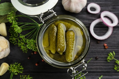 Glass jar of pickled cucumbers on black wooden table, flat lay