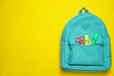 Stylish backpack with different school stationary on yellow background, top view. Space for text