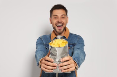 Handsome man with potato chips against light grey background, focus on hands