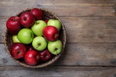 Photo of Fresh ripe green and red apples with water drops in wicker bowl on wooden table, top view. Space for text