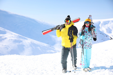 Young couple with skis on hill, space for text. Winter vacation