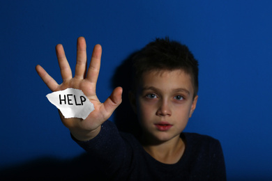 Abused little boy with sign HELP near blue wall, focus on hand. Domestic violence concept