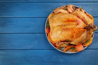 Roasted chicken with oranges on blue wooden table, top view. Space for text