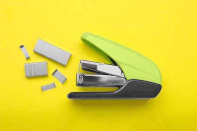 Photo of New bright stapler with staples on yellow background, fat lay. School stationery