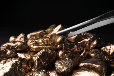 Tweezers with gold nugget above pile against black background, closeup