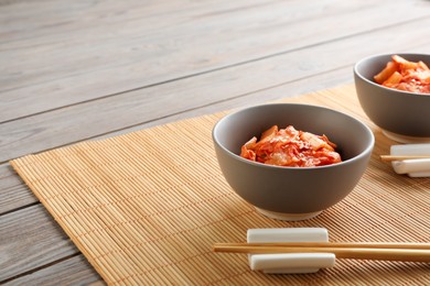 Photo of Bowls of spicy cabbage kimchi and chopsticks on wooden table