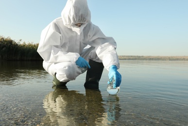 Scientist in chemical protective suit with florence flask taking sample from river for analysis